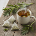Mugwort herbal tea bags beside a steaming mug with fresh mugwort leaf sprigs, no flowers