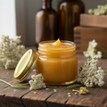 Yarrow beeswax salve in a clear glass jar with a gold lid, with honeycomb and dried yarrow flowers