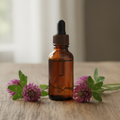 Plain amber glass dropper bottle of red clover tincture with red clover blossoms on a wooden surface